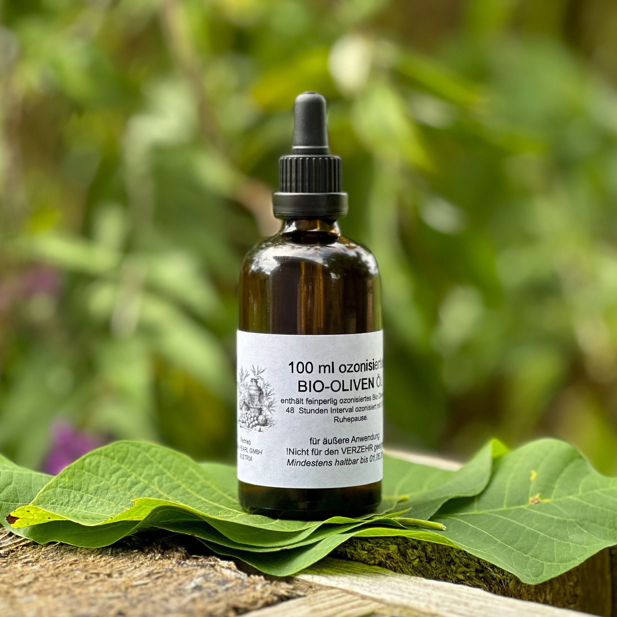 Braune Glasflasche mit schwarzem Tropfer, auf Blättern. Etikett mit Text: BIO-OLIVEN ÖL, 100 ml. Für äußere Anwendung.