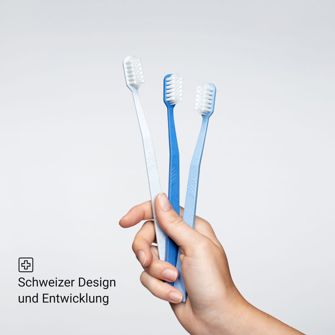 Drei blaue Zahnbürsten in verschiedenen Blautönen. In einer Hand gehalten.