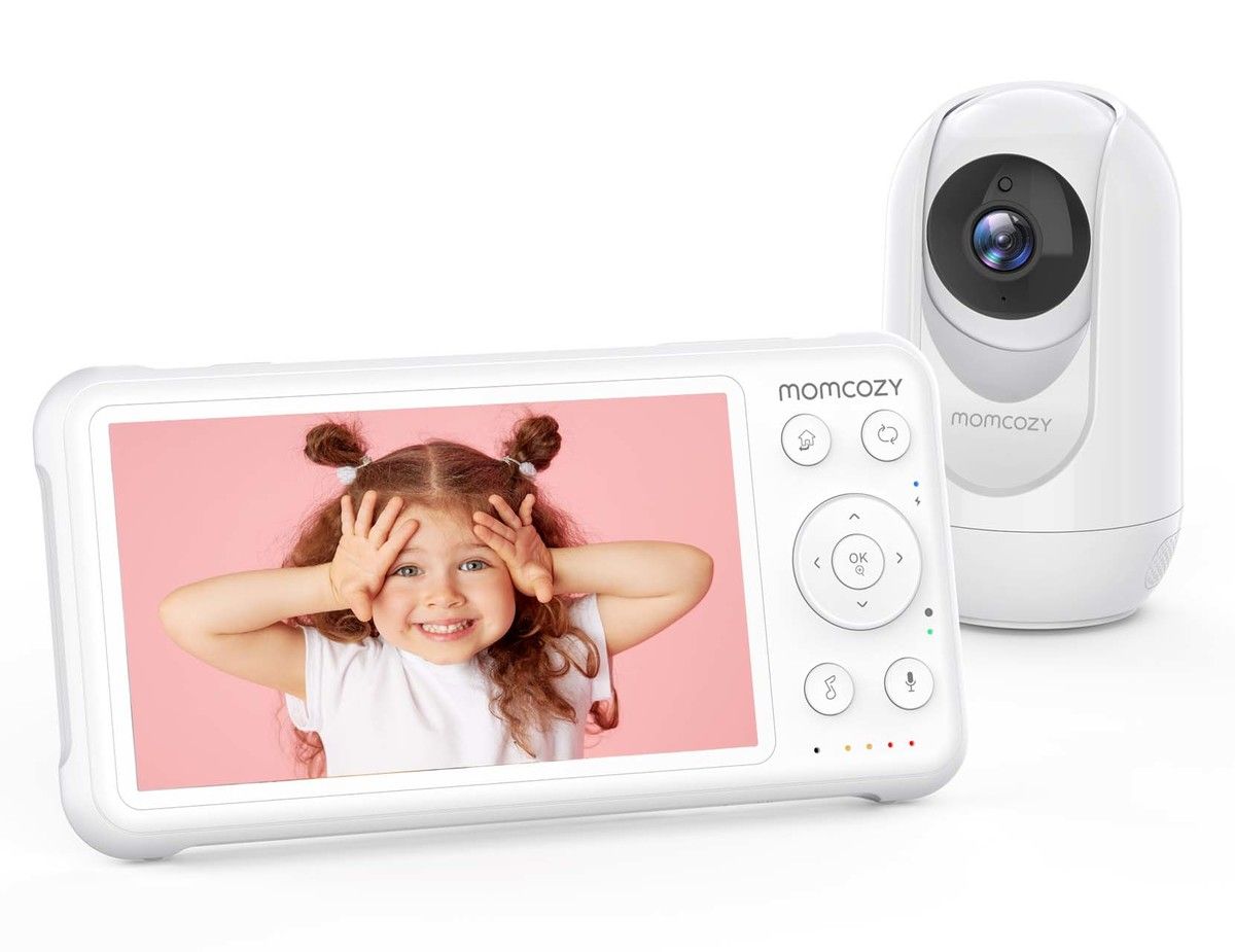 Il baby monitor Momcozy mostra un bambino sorridente sullo schermo. Il dispositivo è bianco e ha pulsanti. Accanto c'è una telecamera bianca. Il baby monitor ha il logo Momcozy.