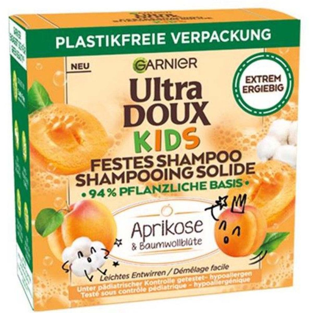 Kartonverpackung mit Garnier Ultra Doux Kids festes Shampoo. Aprikose & Baumwollblüte. Grün-orangefarbenes Design. Text: Plastikfreie Verpackung.