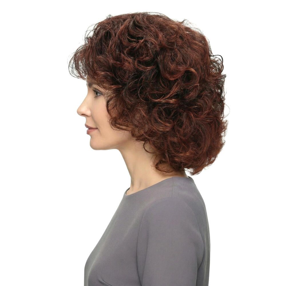 Frau mit brauner, lockiger Perücke. Seitenansicht. Graues Oberteil. Weißer Hintergrund.