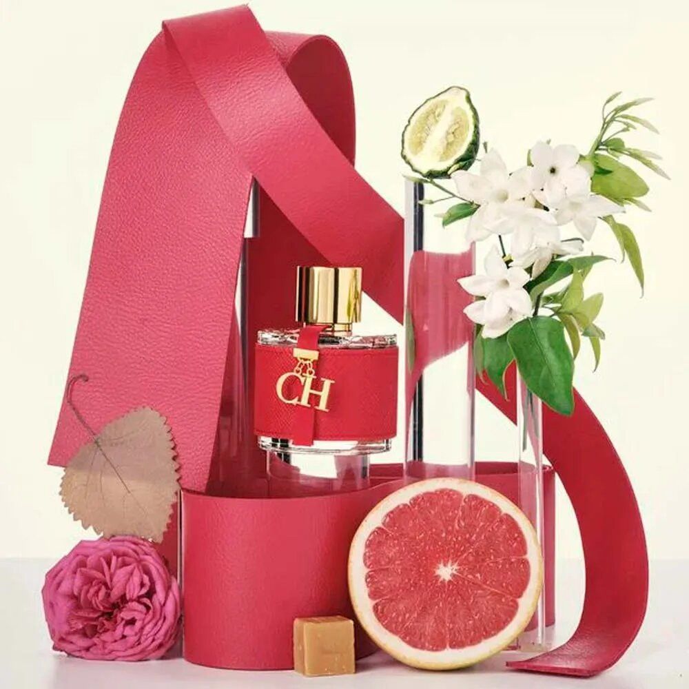 Roter Flakon mit goldfarbenem Verschluss und Anhänger. Dekoration mit roten Bändern, Blumen, Grapefruit und Zitrone.