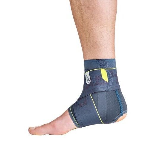 Knöchelbandage am Fuß. Grau-blaue Farbe mit gelben Akzenten. Klettverschluss und Logo sichtbar.