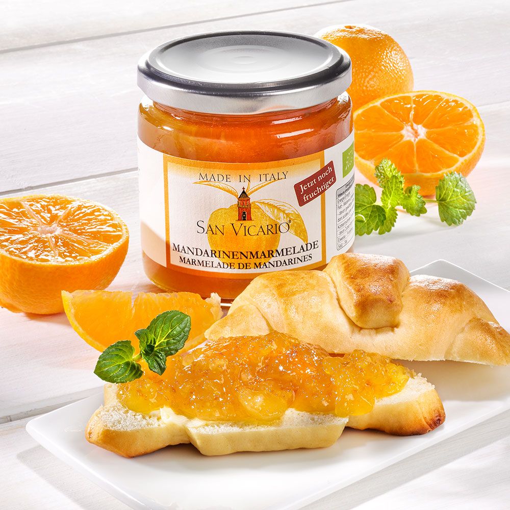 Glas Mandarinenmarmelade auf einem Tisch. Aufgeschnittenen Mandarinen, Brot mit Marmelade, Minze. Etikett "San Vicario".