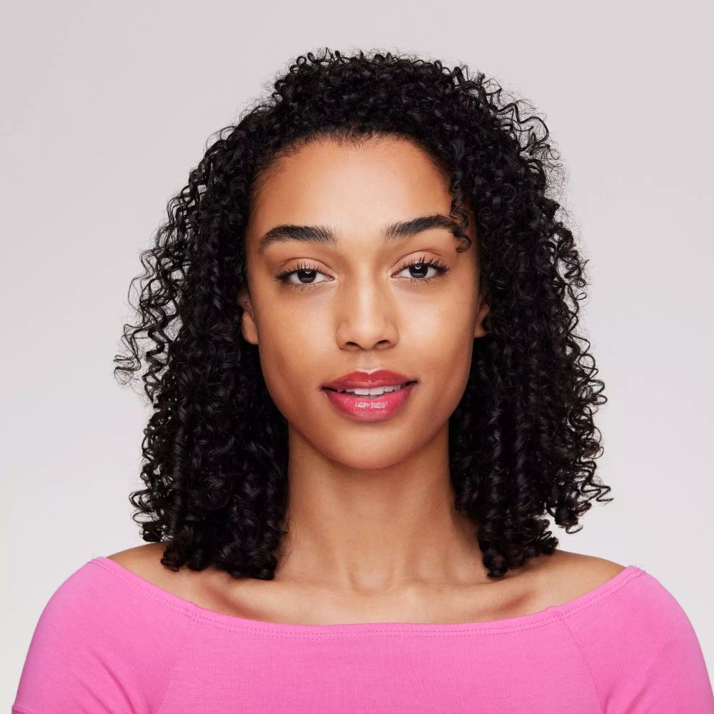 Porträt einer Frau mit lockigem Haar. Sie trägt einen rosa Lippenstift. Der Hintergrund ist hellgrau.