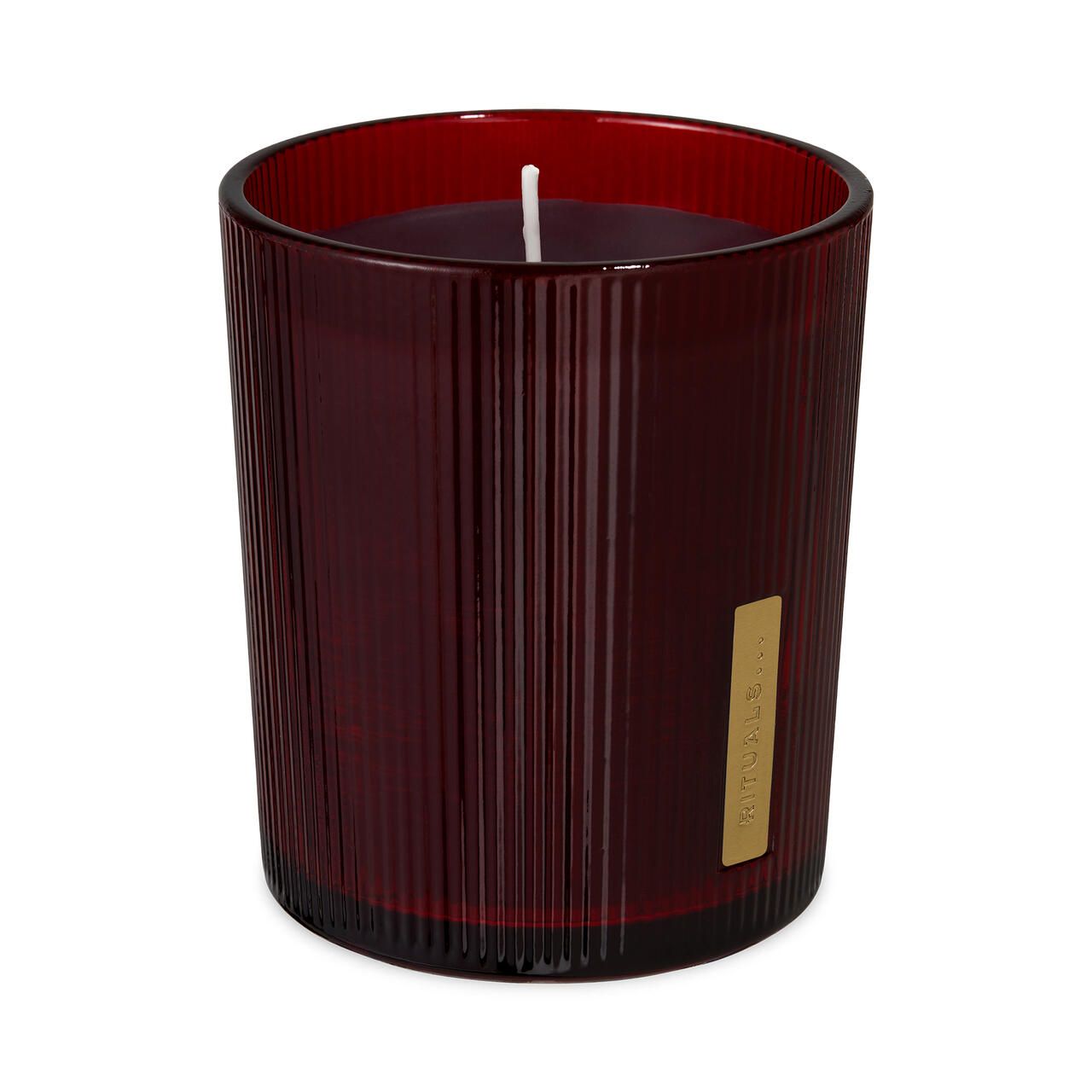 Rote Duftkerze in gerilltem Glas. Kleines goldenes Etikett. Weißer Docht. Auf weißem Hintergrund.