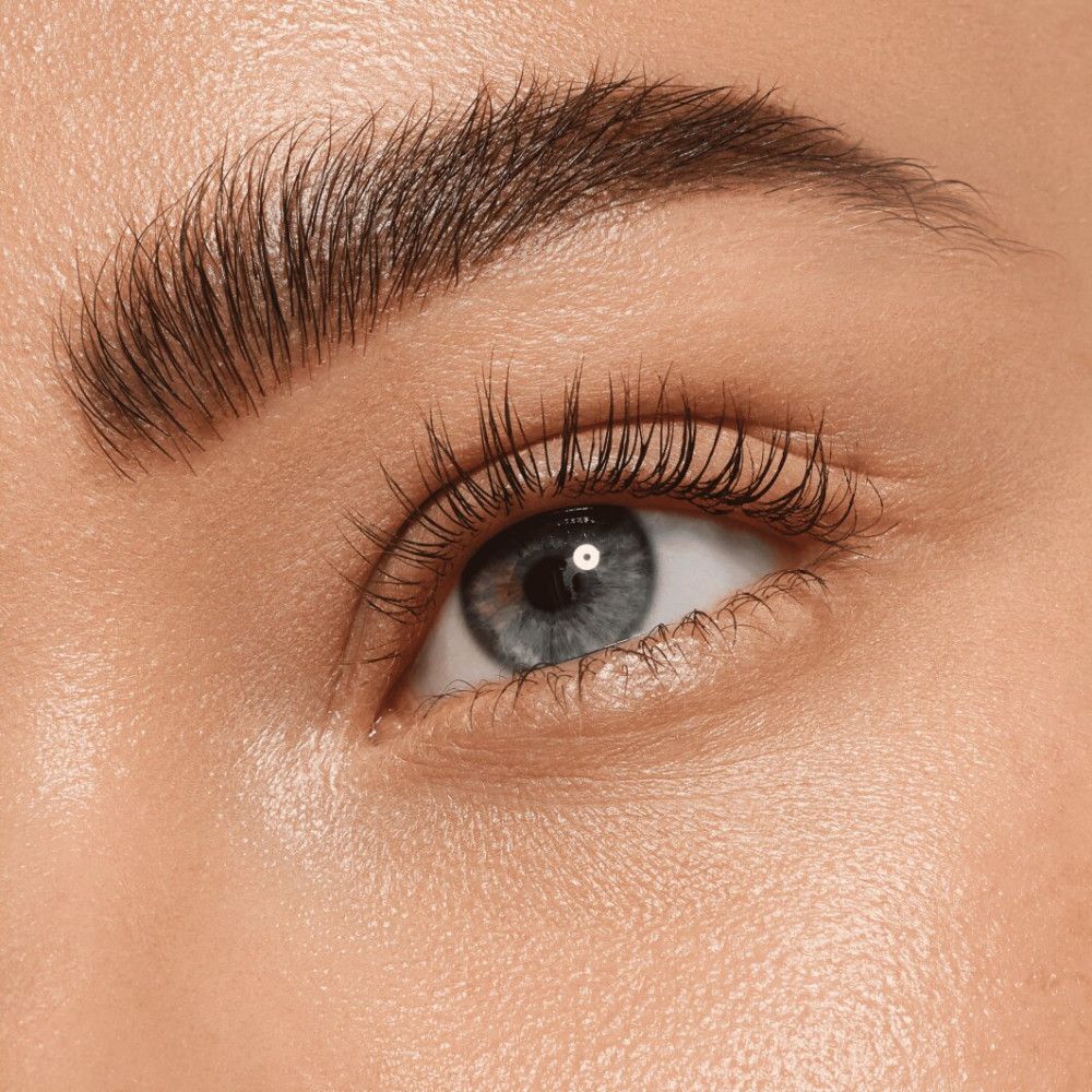 Nahaufnahme eines Auges mit Augenbrauen. Augenbraue geformt und gefärbt. Blaue Augenfarbe. Wimpern betont.