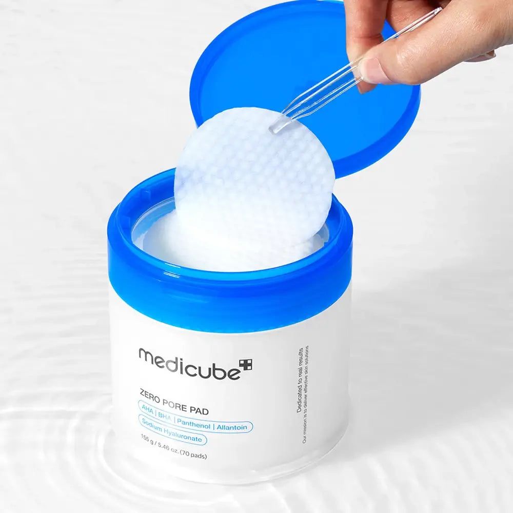 Behälter Medicube Zero Pore Pad mit blauem Deckel. Ein Pad wird aus dem Behälter entnommen. Text: Zero Pore Pad, Inhaltsstoffe. 70 Pads.