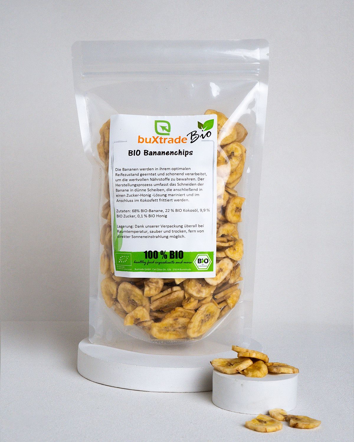 Transparente Tüte mit Bio Bananenchips. Aufkleber mit Produktinformationen. Die Tüte steht auf einem weißen Podest.