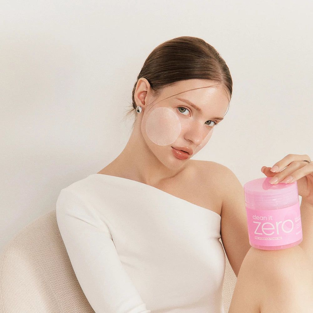Eine Frau hält einen rosa Behälter mit der Aufschrift "Clean it Zero". Auf ihrem Gesicht befinden sich Pads.