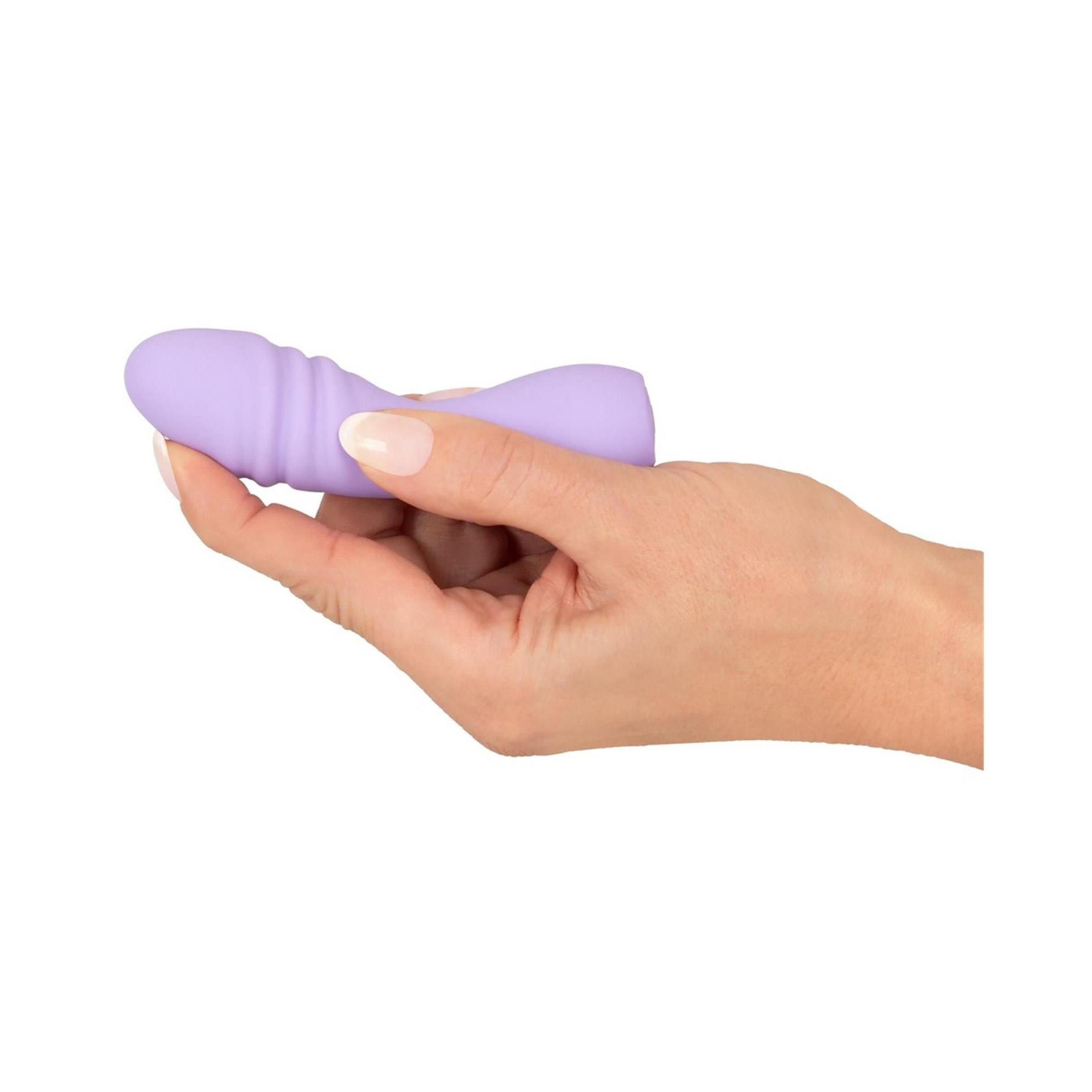 Lila Vibrator in Hand gehalten. Längliche Form, gewellte Oberfläche. Material: Silikon.