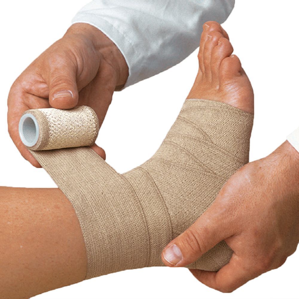 Person wickelt einen Verband um den Knöchel einer anderen Person. Der Verband ist beige und wird von einer Rolle abgewickelt.