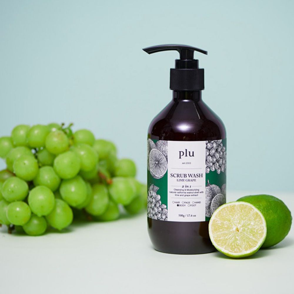 Braune Flasche mit schwarzem Pumpverschluss, neben Limetten und Trauben. Etikett: plu, Scrub Wash Lime Grape. Auf hellem Hintergrund.