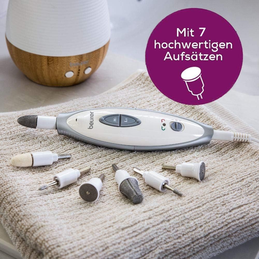 Elektrische Nagelfeile mit 7 Aufsätzen. Weißes Gehäuse mit grauen Bedienelementen. Aufsätze liegen auf einem Handtuch.