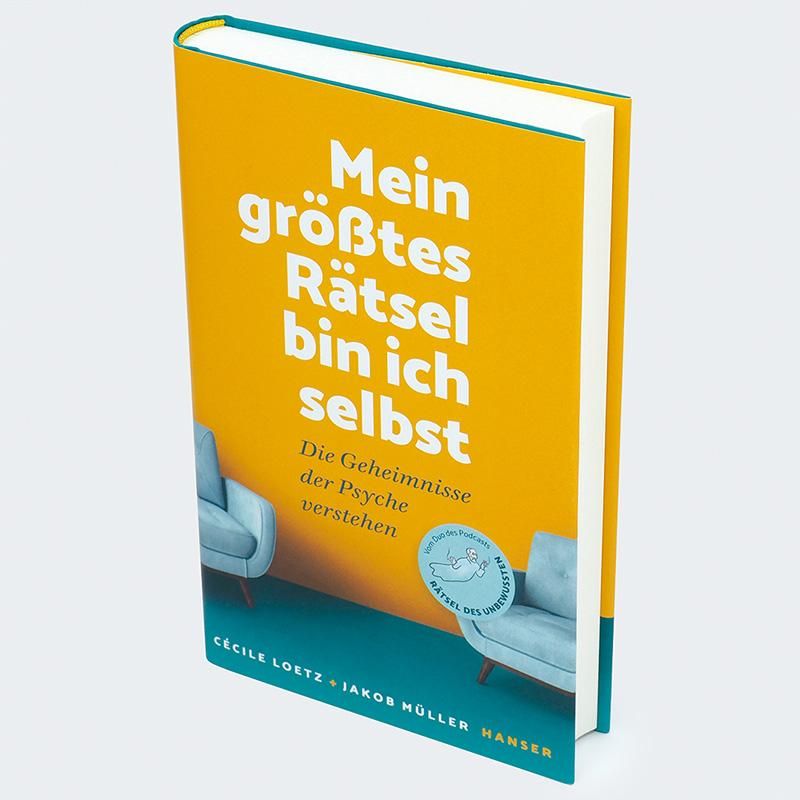 Buch "Mein größtes Rätsel bin ich selbst" im 3/4-Winkel. Gelbes Cover, weißer Titel. Blaue Sessel. Grüner Buchrücken. Hanser-Verlag.