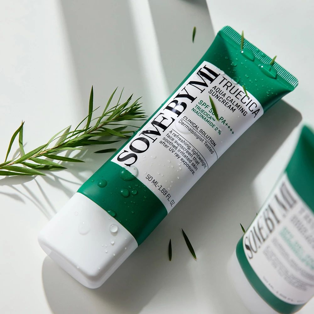 Grüne und weiße Tube mit Sonnencreme. Text: SOMEBYMI, Truecica Aqua Calming Suncream, SPF 50+ PA++++. Blätter liegen daneben.