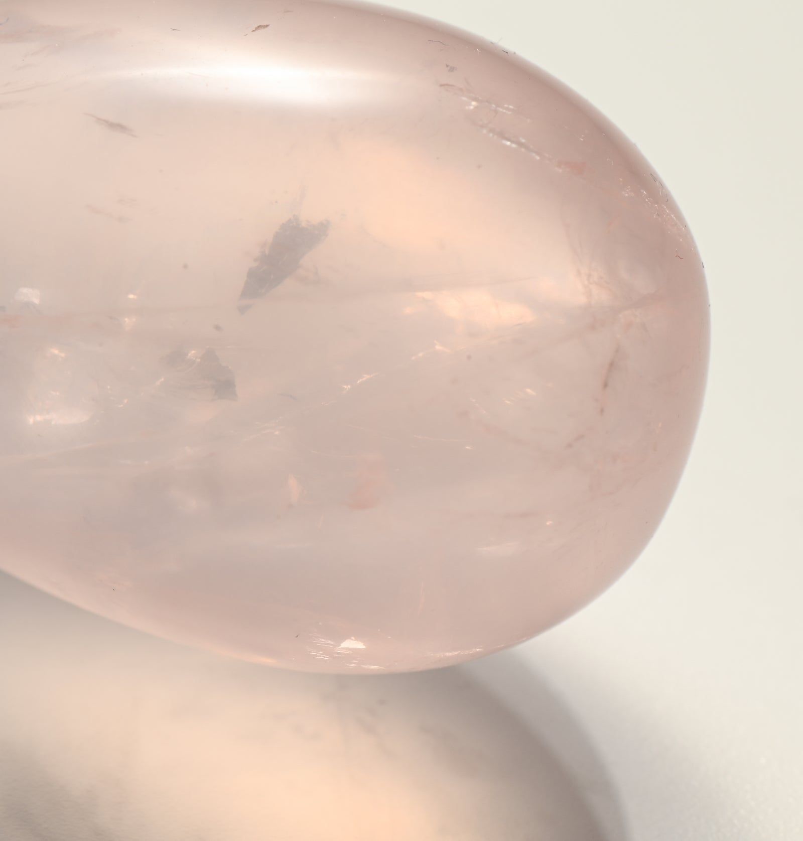 Nahaufnahme eines rosafarbenen Yoni-Eis aus Stein. Die Oberfläche ist leicht transparent und weist natürliche Einschlüsse auf.