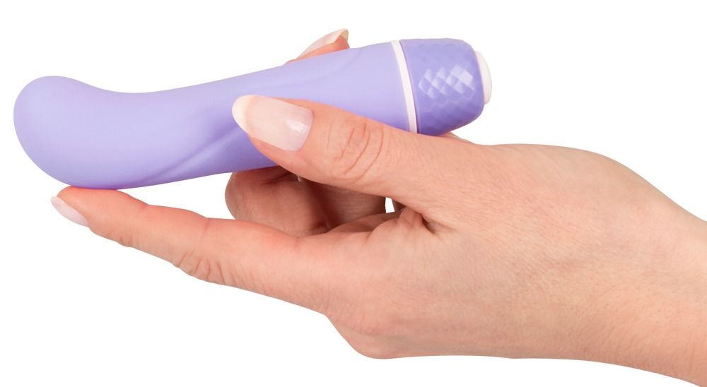 Hand hält lila Vibrator. Gebogene Form, abgerundete Spitze. Weißer Sockel mit facettiertem Muster.