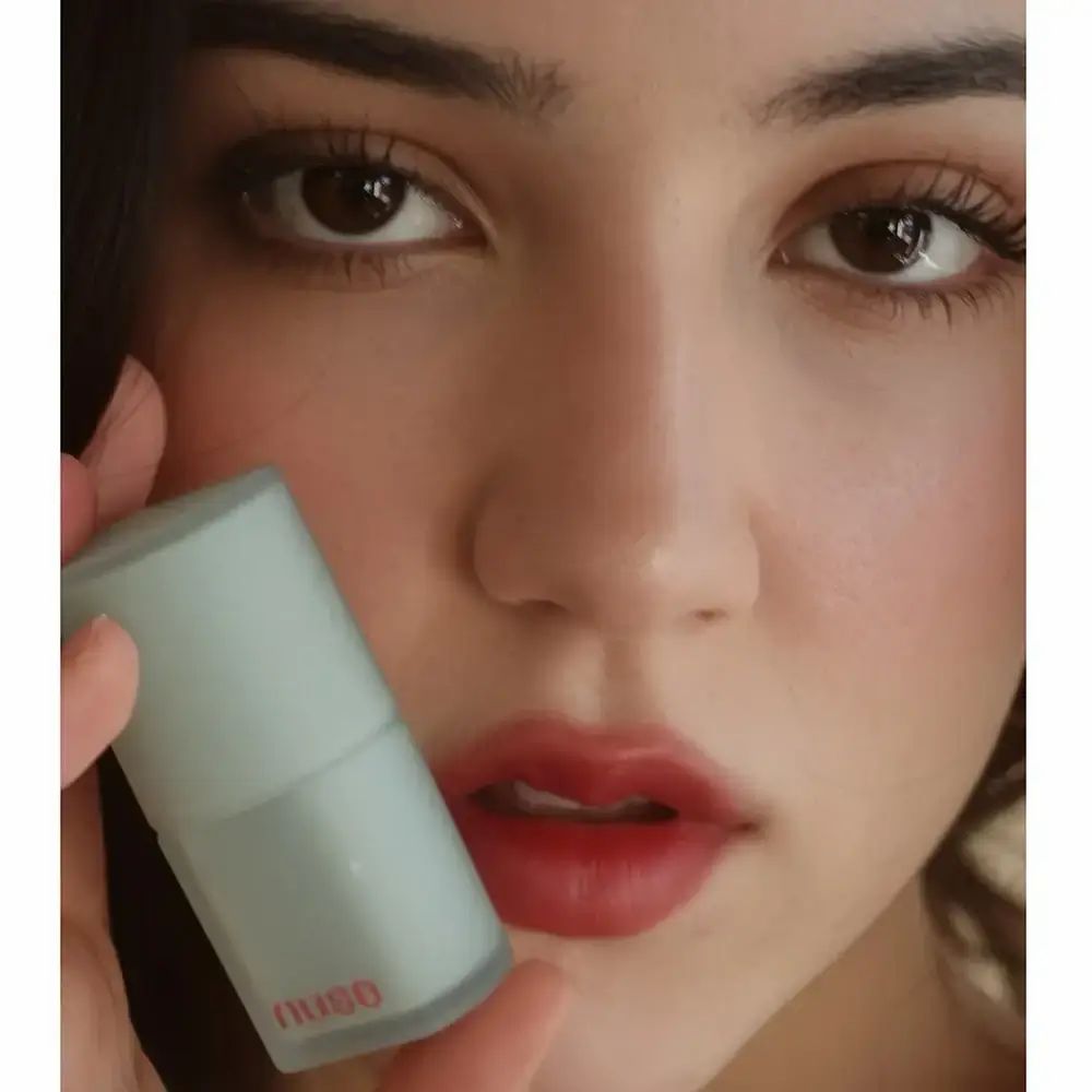 Frau hält eine Lippenstift-Verpackung. Die Lippen sind mit Lippenstift bemalt. Der Lippenstift ist rot.