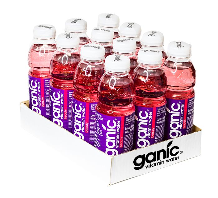 Eine Kiste mit Ganic Vitaminwasser Beauty. Die Flaschen sind aus transparentem Kunststoff mit weißen Deckeln. Das Etikett ist lila mit weißer Schrift. Der Karton ist weiß und trägt den Markennamen.
