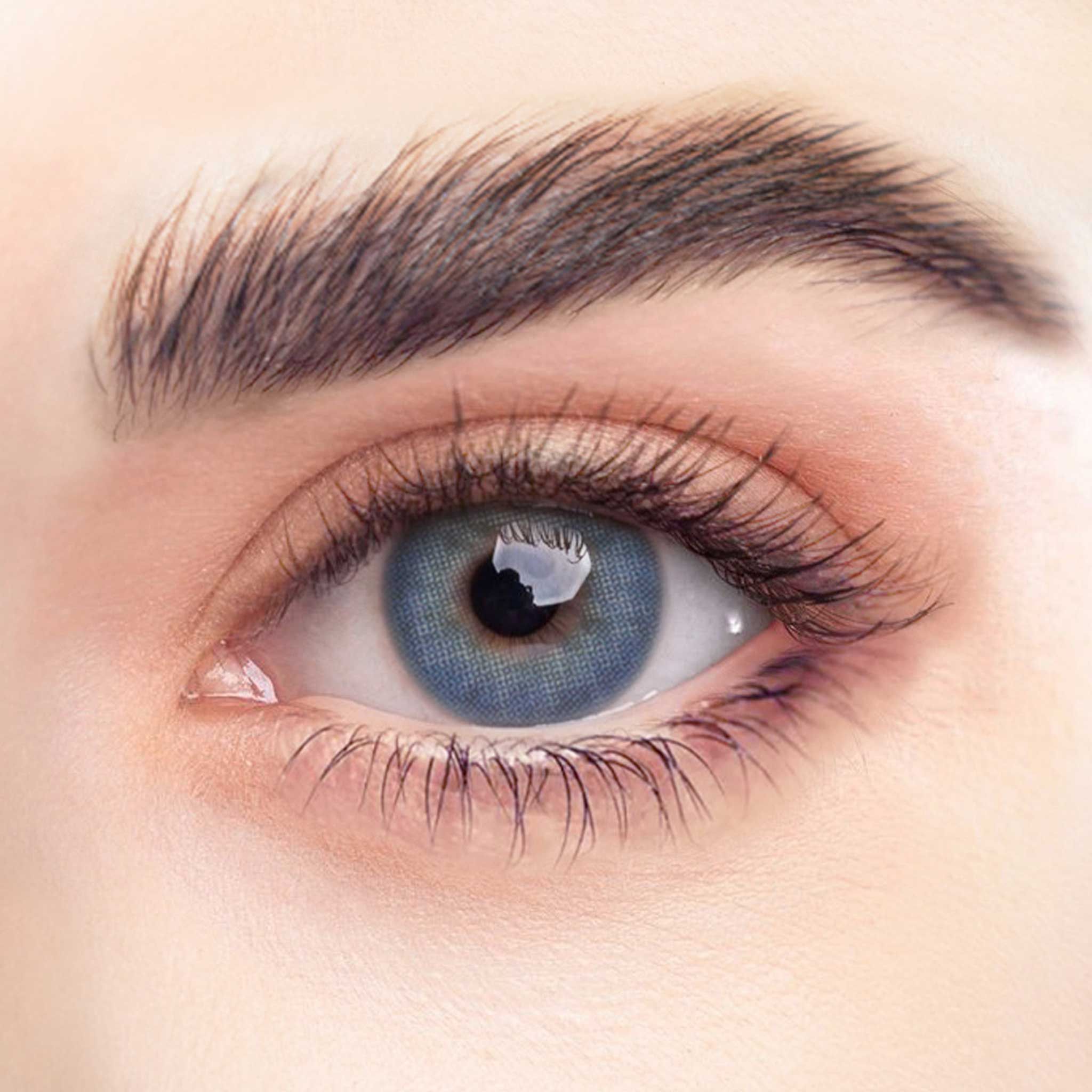 Nahaufnahme eines Auges mit blauer Kontaktlinse. Die Iris ist blau, die Pupille schwarz. Lange Wimpern umranden das Auge.