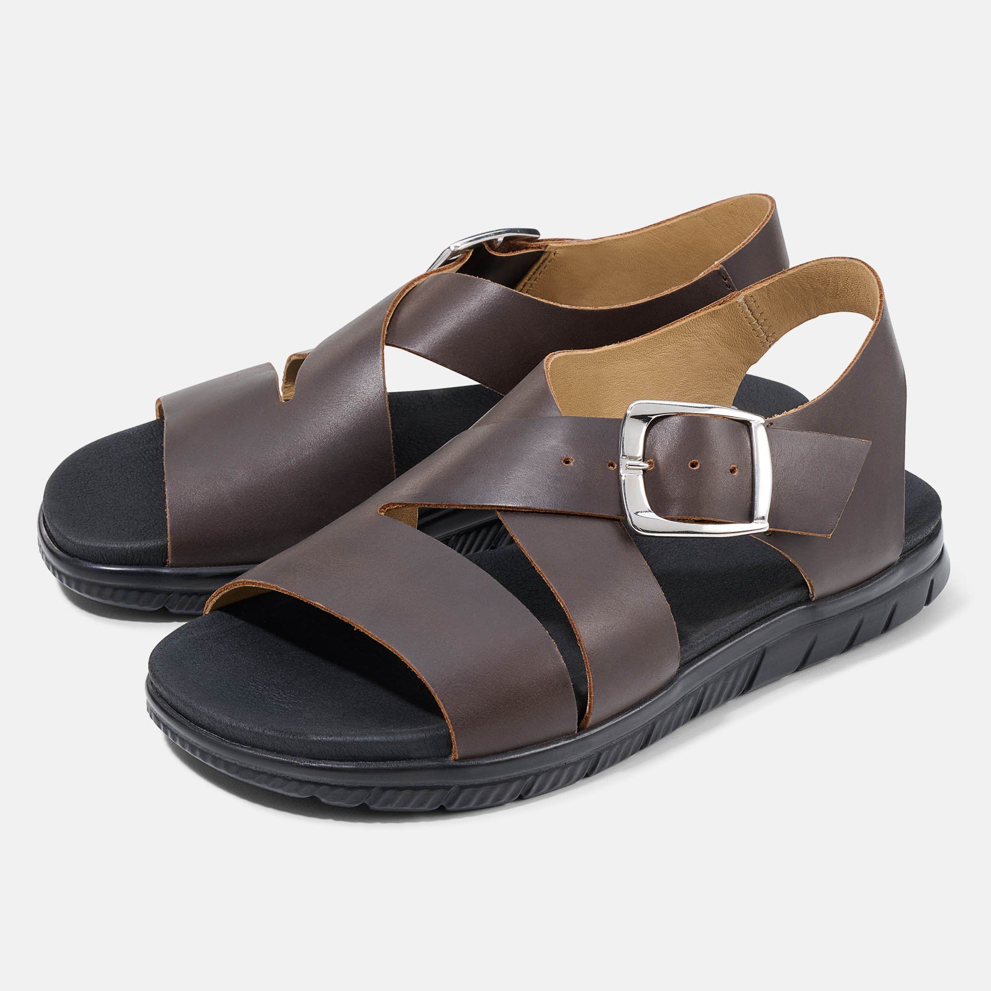 Braune Sandalen mit schwarzen Sohlen. Kreuzriemen, silberne Schnalle. Zwei Schuhe nebeneinander.