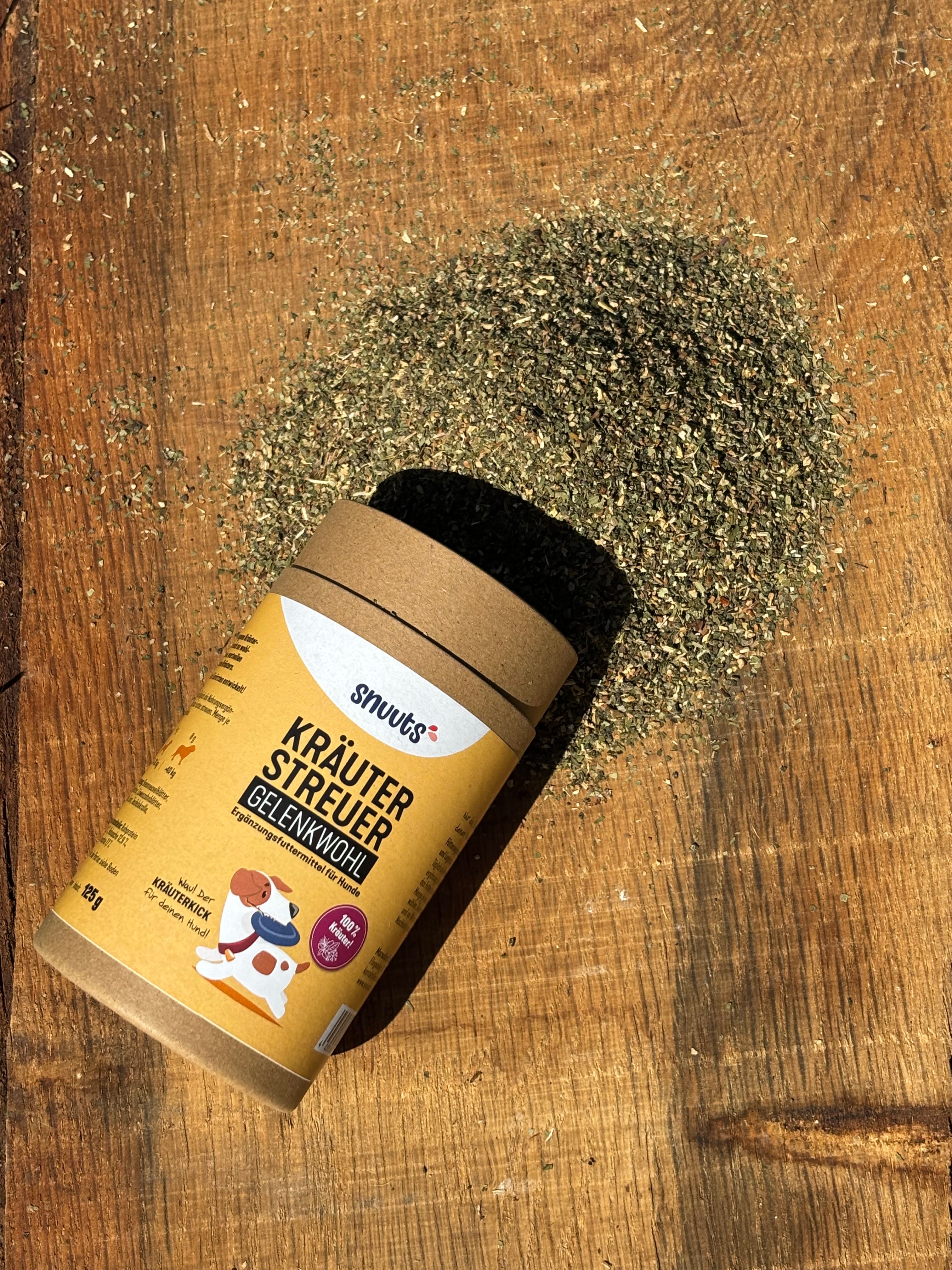 Zylindrische Dose und Kräuter auf Holz. Dose: snuuts Kräuterstreuer Gelenkwohl. Kräuterhaufen daneben. Schatten.