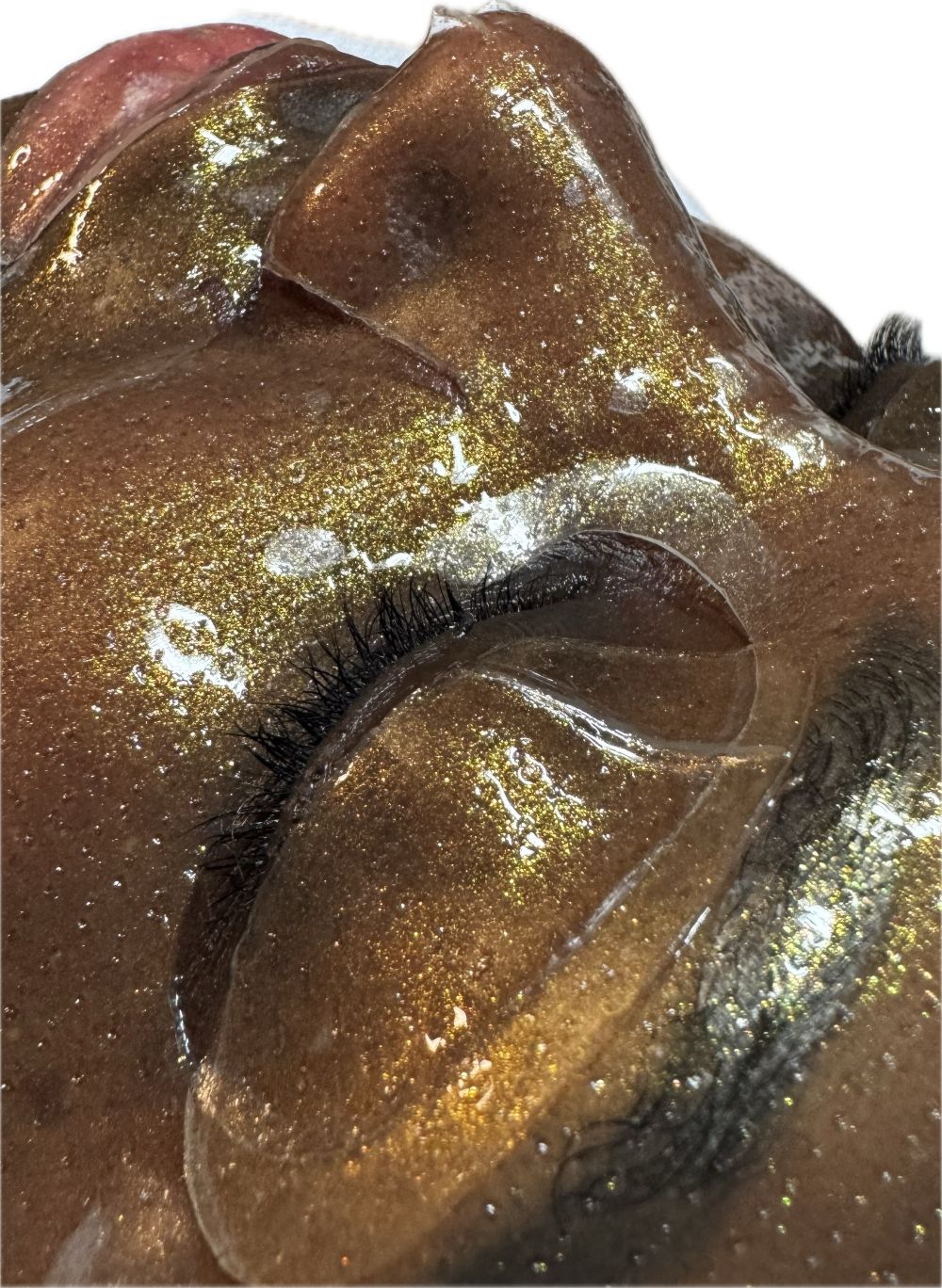 Nahaufnahme eines Gesichts mit aufgetragener Gesichtsmaske. Die Maske ist goldfarben und bedeckt das Gesicht. Augenpartie sichtbar.