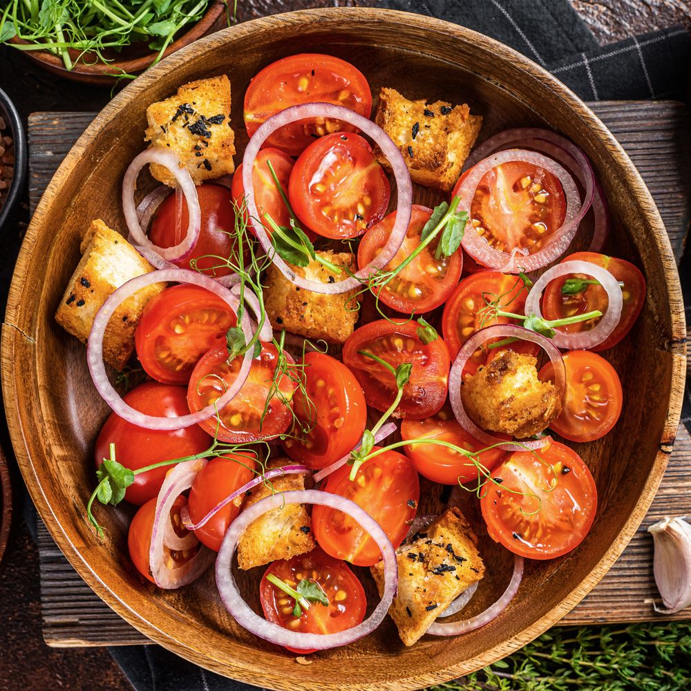 Holzschale mit Tomaten, Zwiebeln und Croutons. Draufsicht. Dunkler Hintergrund.