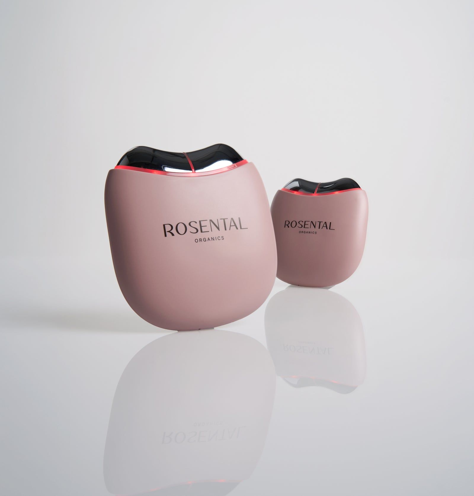 Zwei rosa Geräte mit der Aufschrift "ROSENTAL ORGANICS". Rote Lichter sind sichtbar. Reflektierender Hintergrund.