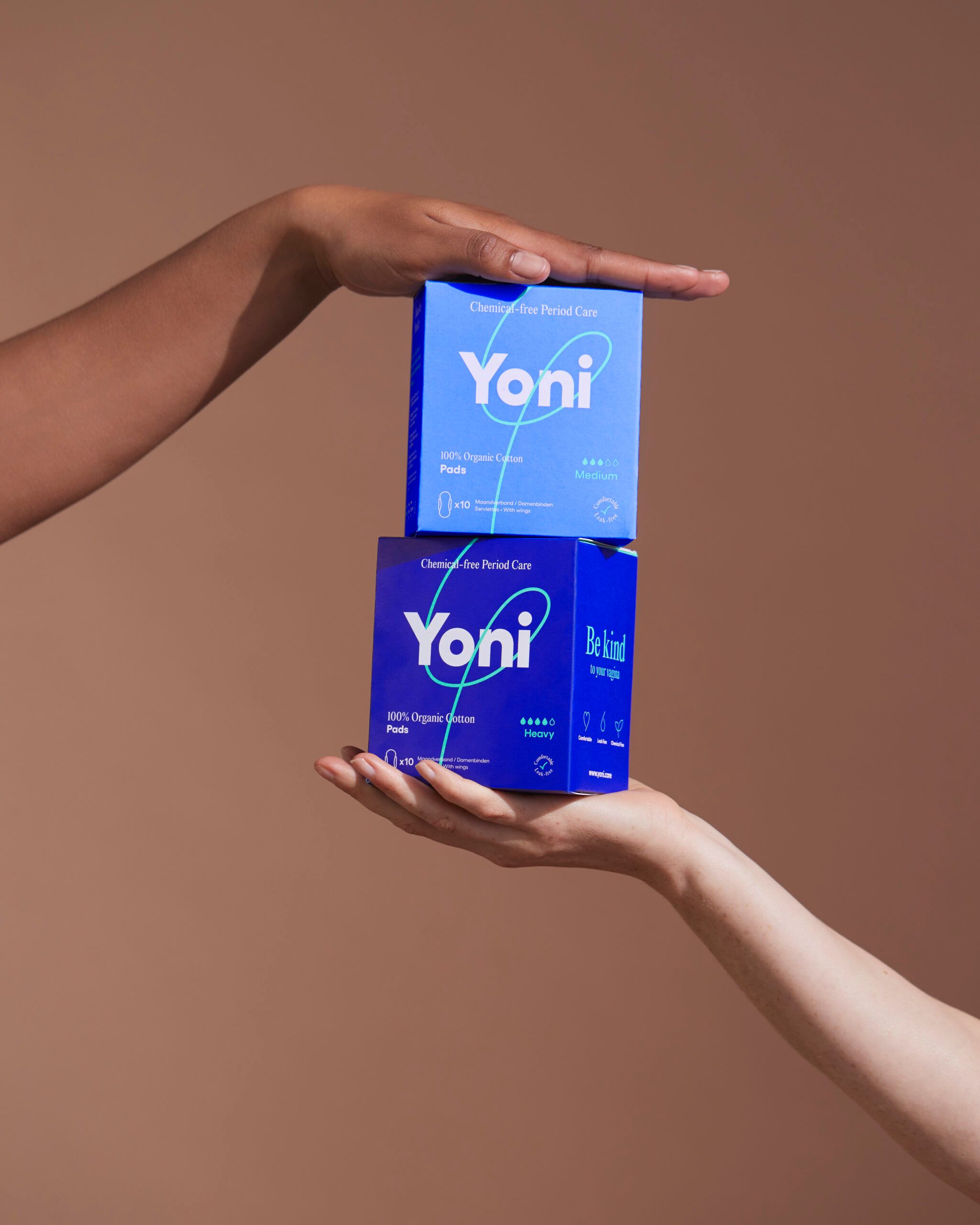 Zwei blaue Schachteln mit Yoni-Logo. Aufschrift: Chemical-free Period Care. Gehalten von Händen.