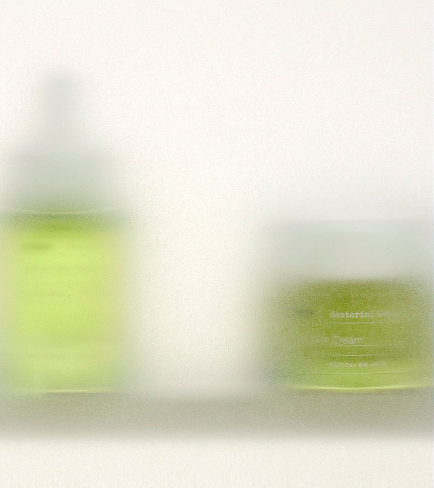 Zwei grüne Kosmetikbehälter, unscharf dargestellt. Ein Flakon mit Pipette und ein Tiegel mit Deckel.