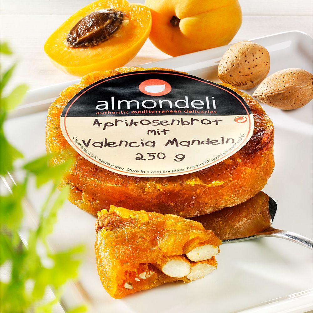 Aprikosenbrot mit Valencia Mandeln, angeschnitten. Auf Teller mit Aprikosen und Mandeln. Marke: almondeli.