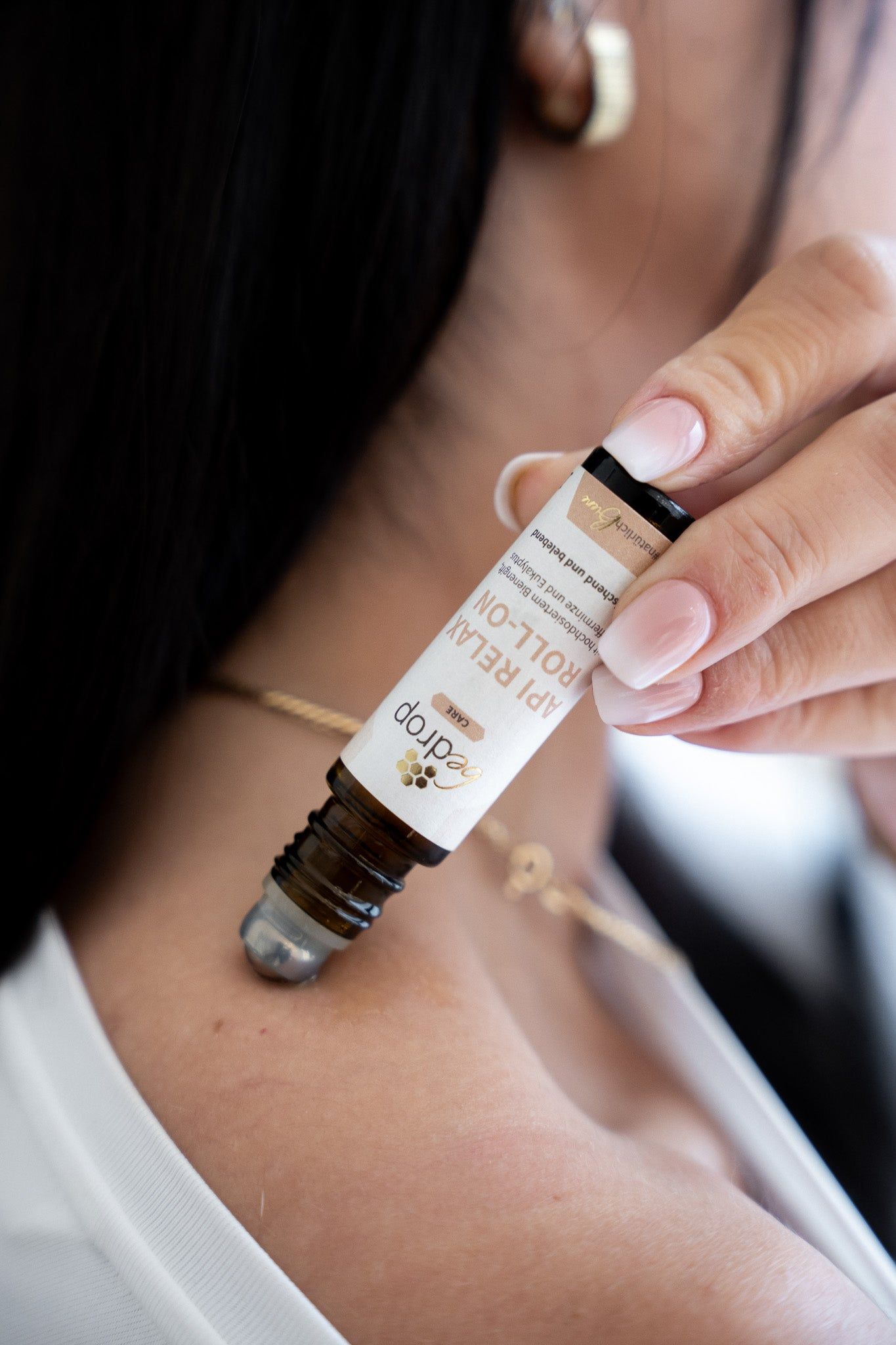 Person hält braune Glasflasche mit schwarzem Deckel. Aufschrift: bedrop API RELAX ROLL-ON. Anwendung am Hals.