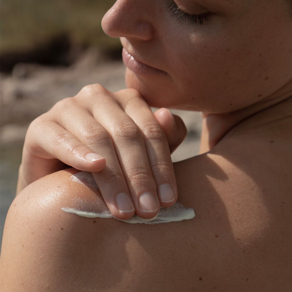 Person trägt Sonnenmilch auf Schulter auf. Creme auf Haut. Tube mit Aufschrift: SONNENMILCH KÖRPER SPF 50+.