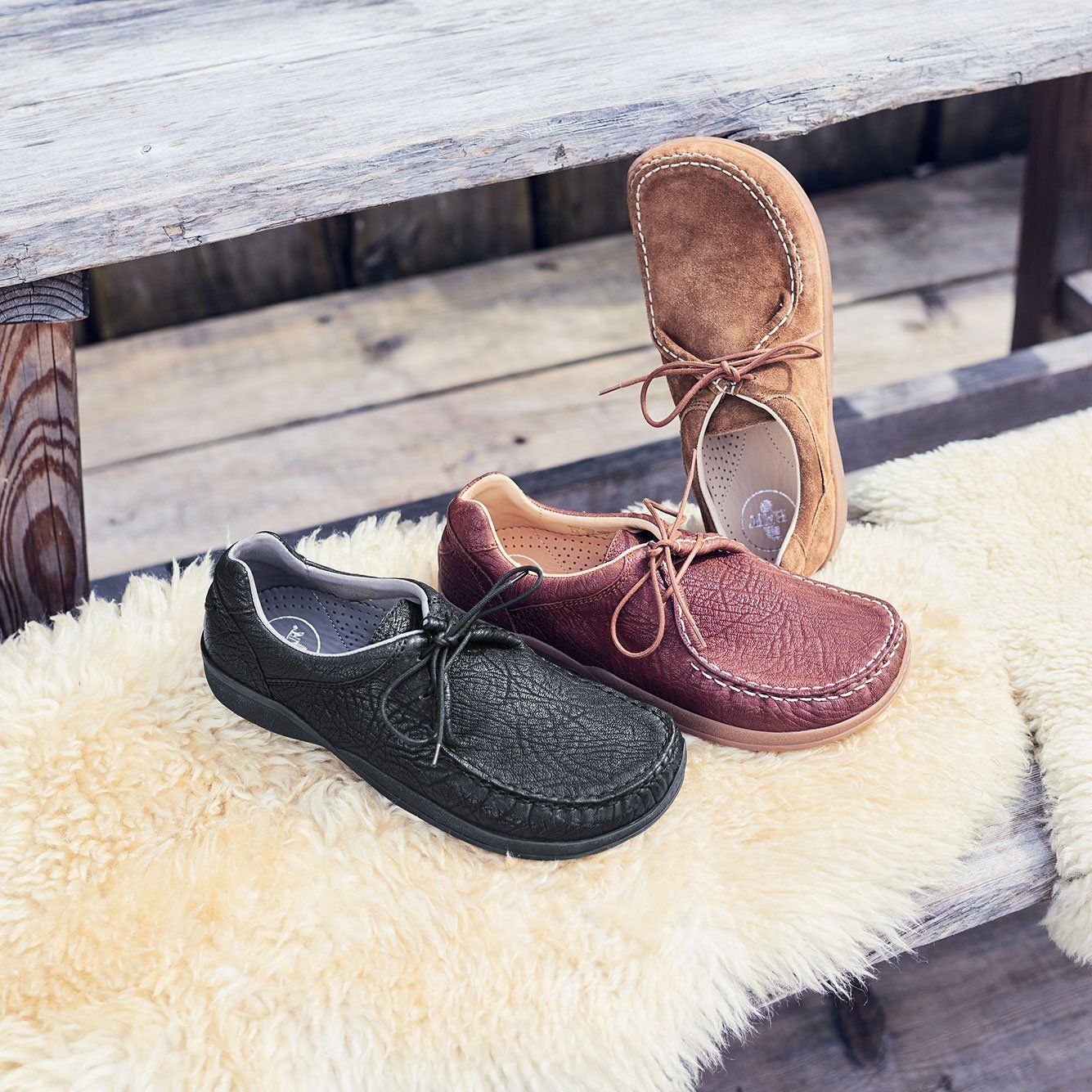 Drei Paar Schuhe auf einer Holzbank. Schwarze, braune und beige Lederschuhe. Schnürsenkel. Verschiedene Farben und Formen.