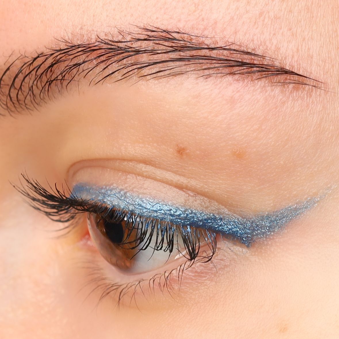 Nahaufnahme eines Auges mit hellblauem Kajal-Eyeliner auf dem oberen Augenlid. Braune Augen mit Wimperntusche.