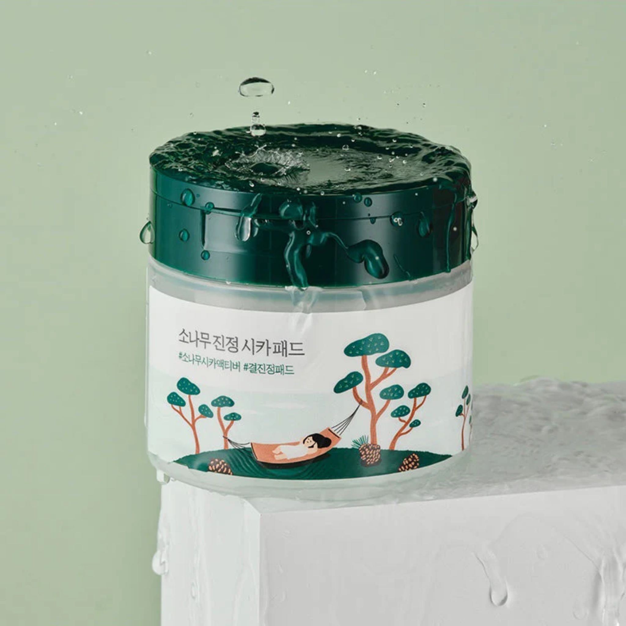 Round Lab Lab Pine Calming Cica Pad: Behälter mit Wassertropfen und Pinien-Cica-Motiv.
