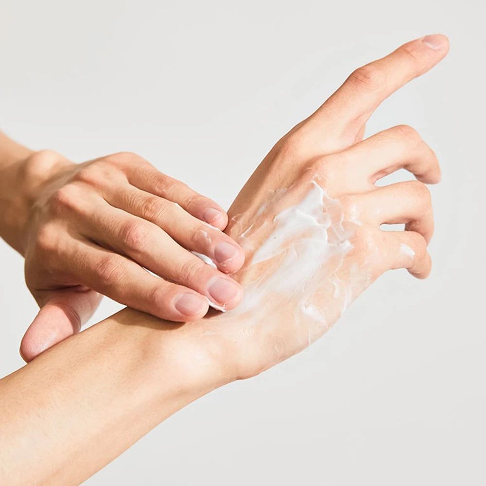Hände, die Creme auf die Haut auftragen. Weiße Creme auf der Hand. Heller Hintergrund.