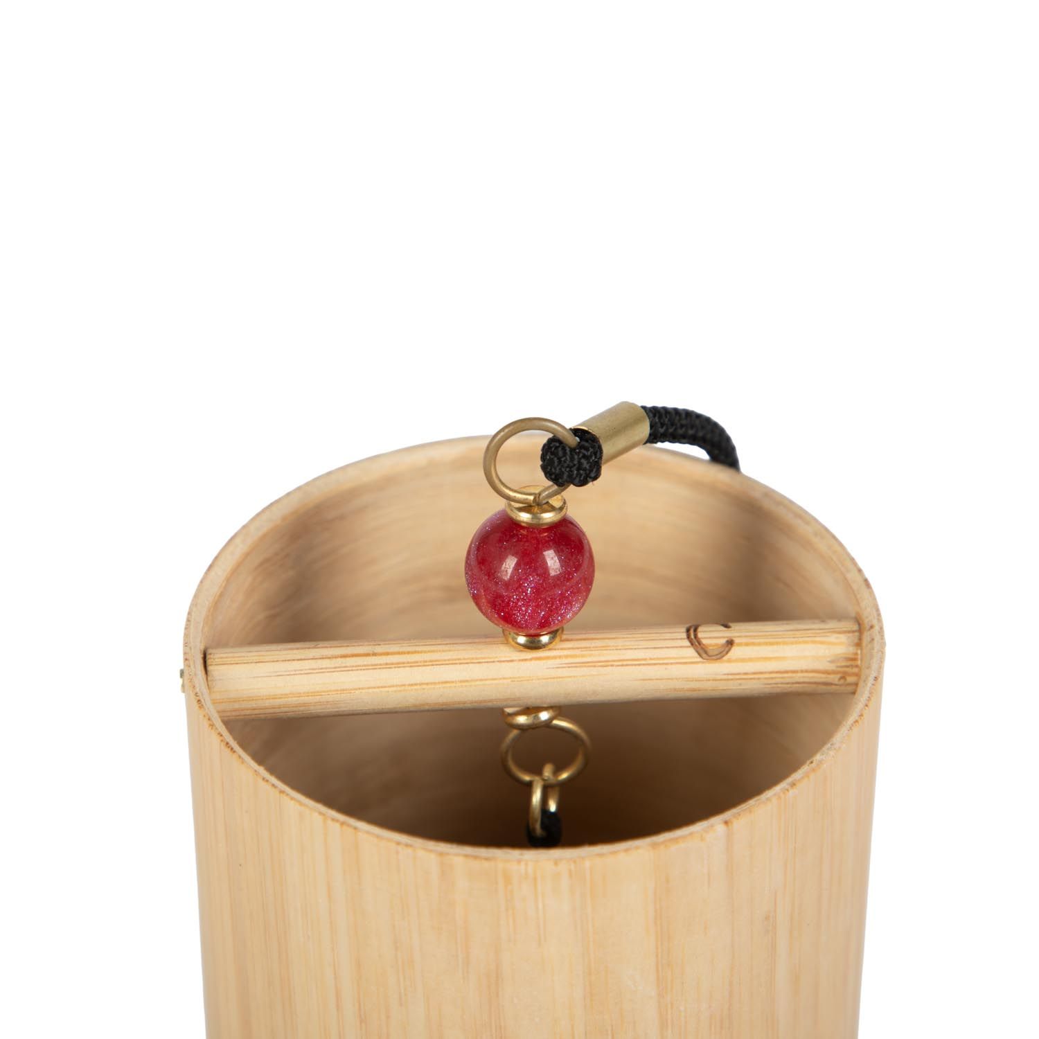 Nahaufnahme des Klangspiels. Bambus-Zylinder mit roter Kugel und Aufhängung. Innenliegende Holzstange. Goldfarbene Ringe.