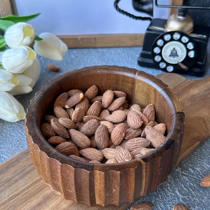Mandeln in einer Holzschale. Die Schale steht auf einem Holzbrett. Im Hintergrund ein Telefon.