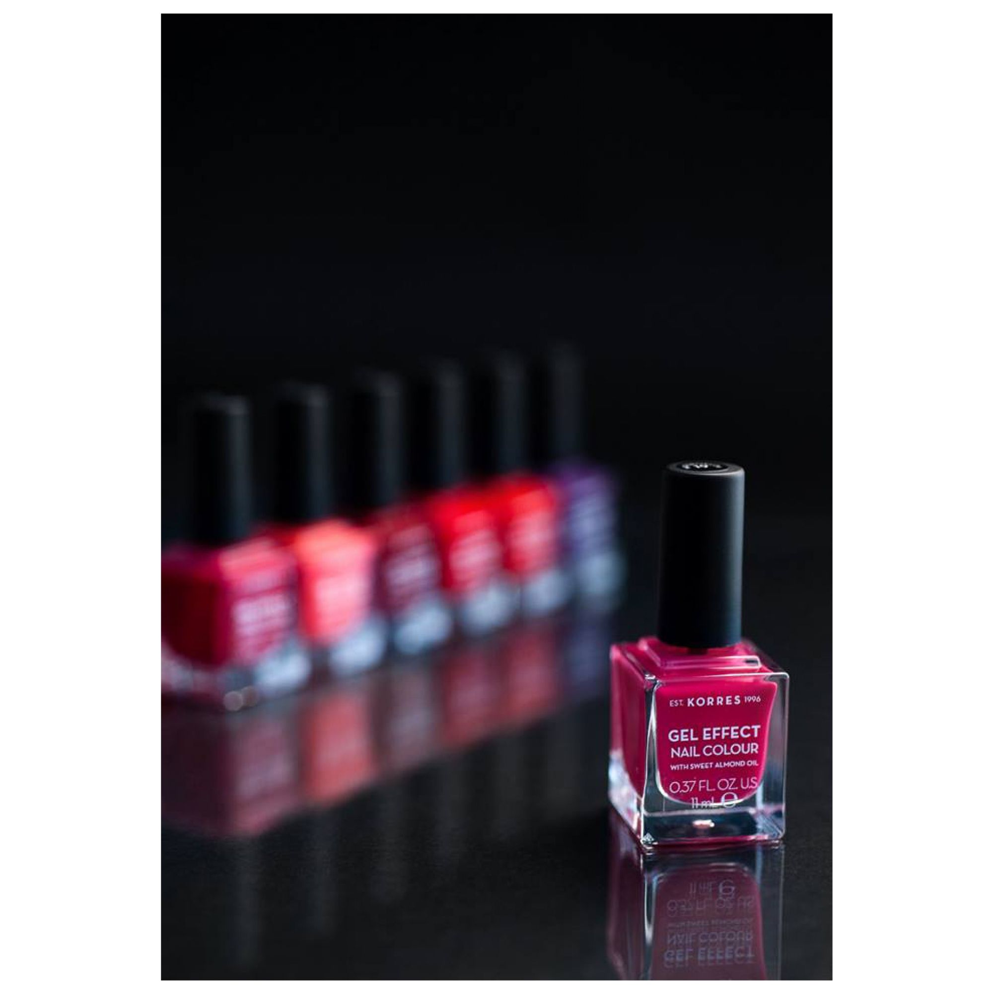KORRES Gel Effect Nagellack in Pink, 0.57 fl oz. Mehrere Flaschen in verschiedenen Rottönen im Hintergrund.