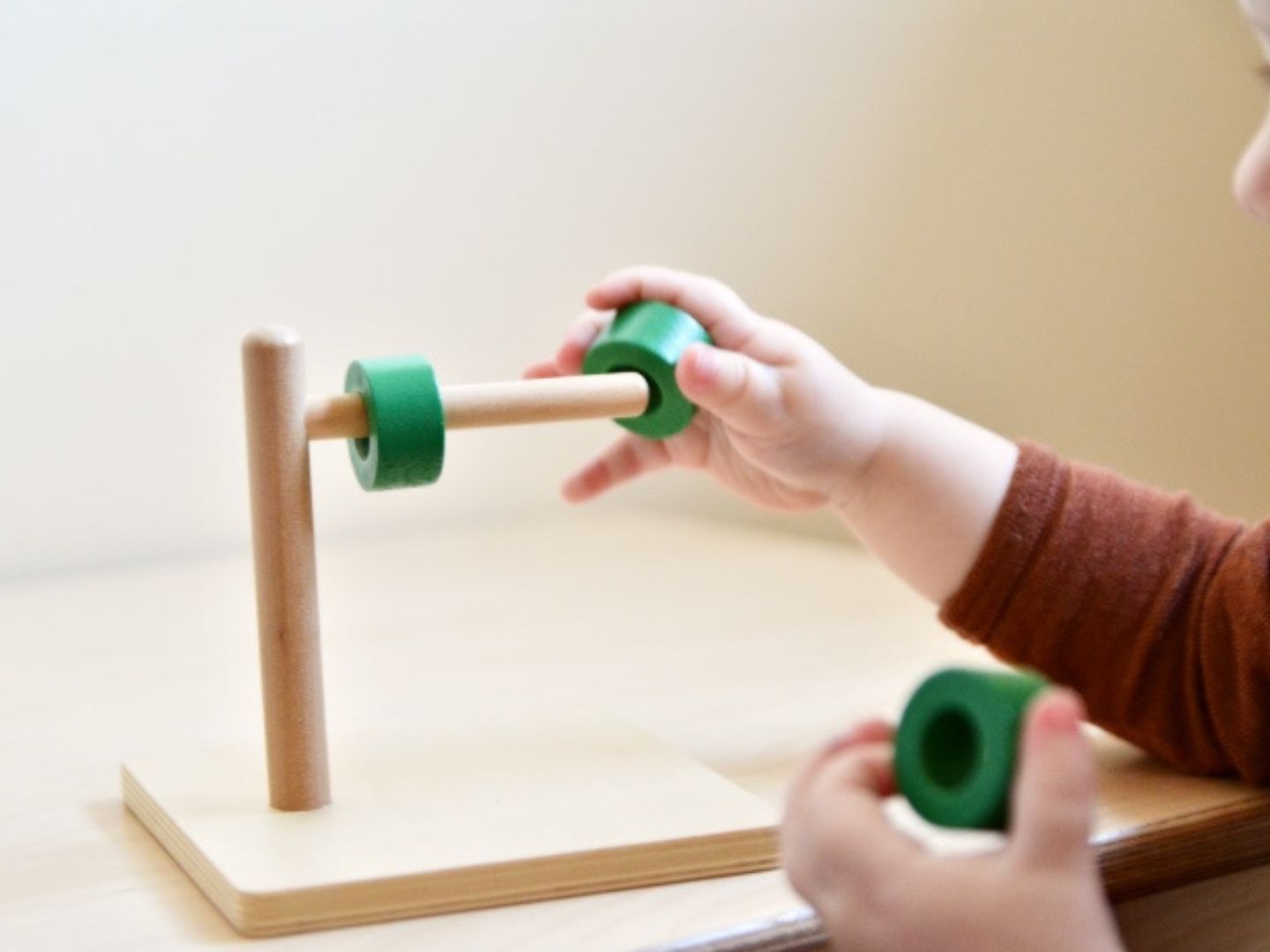 Holzspielzeug mit grünen Ringen und Stäben. Ein Kind spielt damit. Auf einer Holzbasis montiert.