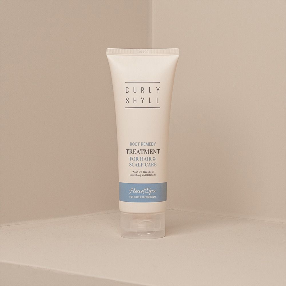 Beige Tube mit Produkttext. Aufschrift: CURLY SHYLL, Root Remedy Treatment, für Haar & Kopfhautpflege. Blaue Leiste: Head Spa. Steht in Ecke.
