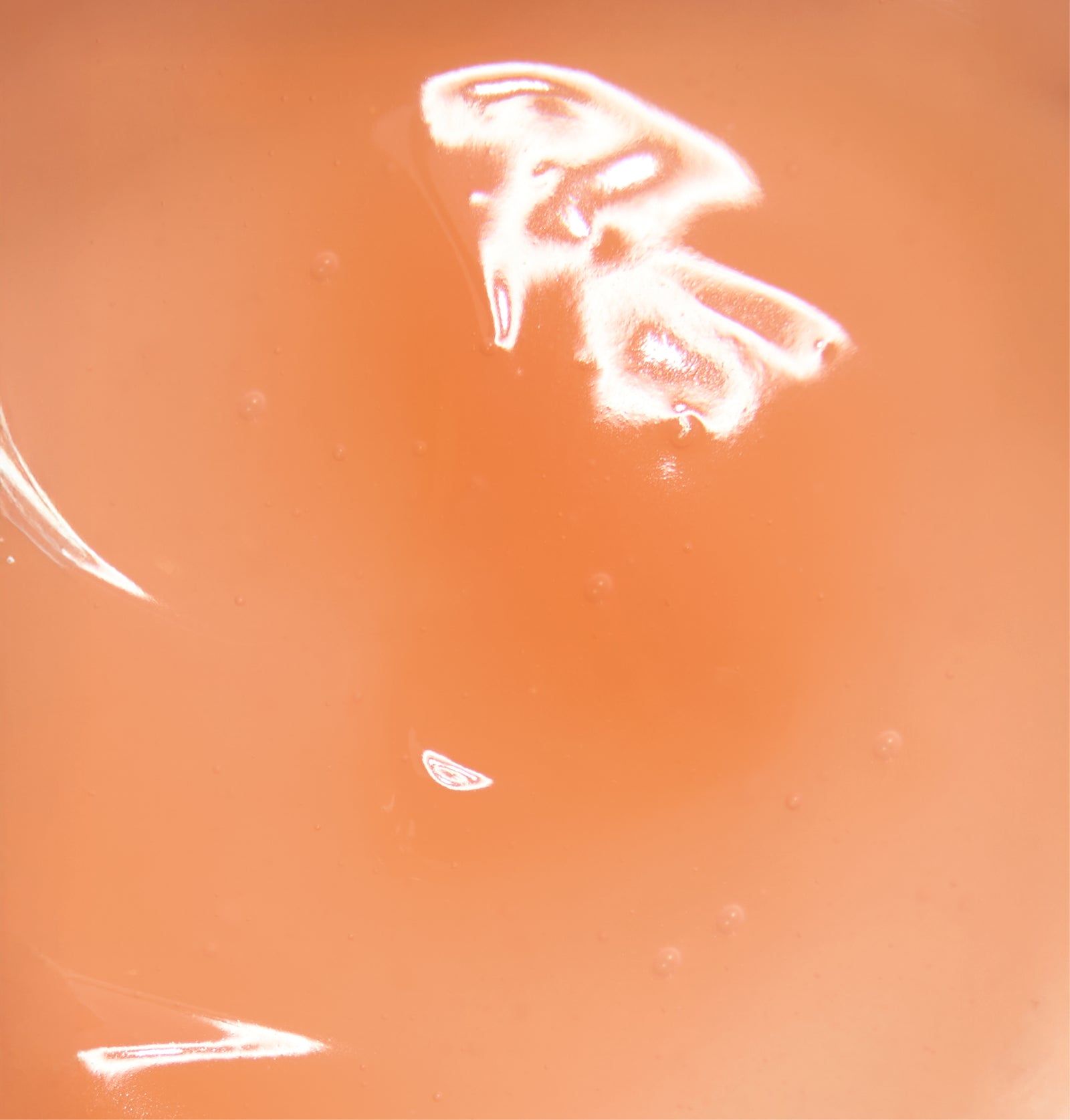 Nahaufnahme einer Flüssigkeit. Orange-rosa Farbton. Glänzende Oberfläche.