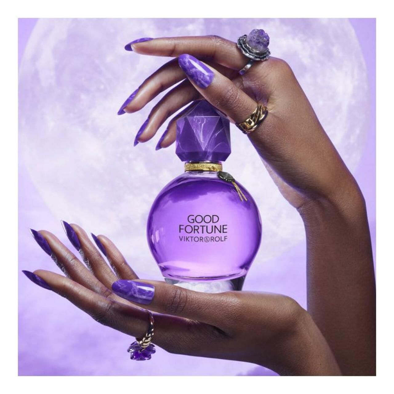 Violetter Flakon mit Kristallverschluss, gehalten von Händen mit Ringen. Aufschrift: Good Fortune, Viktor & Rolf.