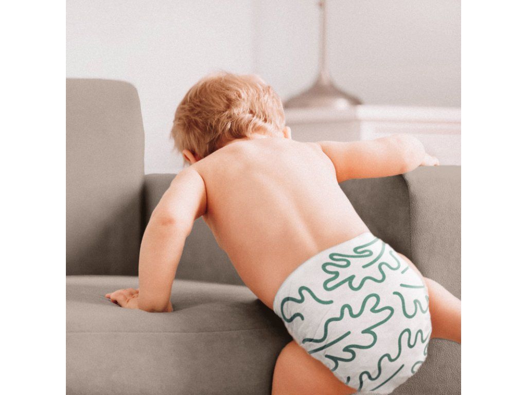 Baby mit Windel, die mit grünen Mustern bedruckt ist, klettert auf ein Sofa.