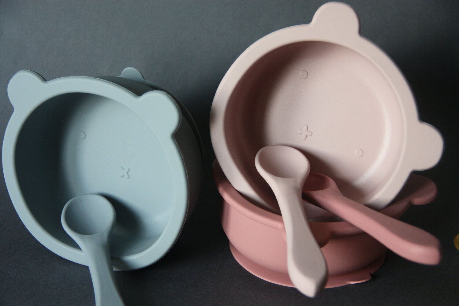 Zwei Schüsseln mit Löffeln. Rosa und hellblau. Auf grauem Hintergrund.