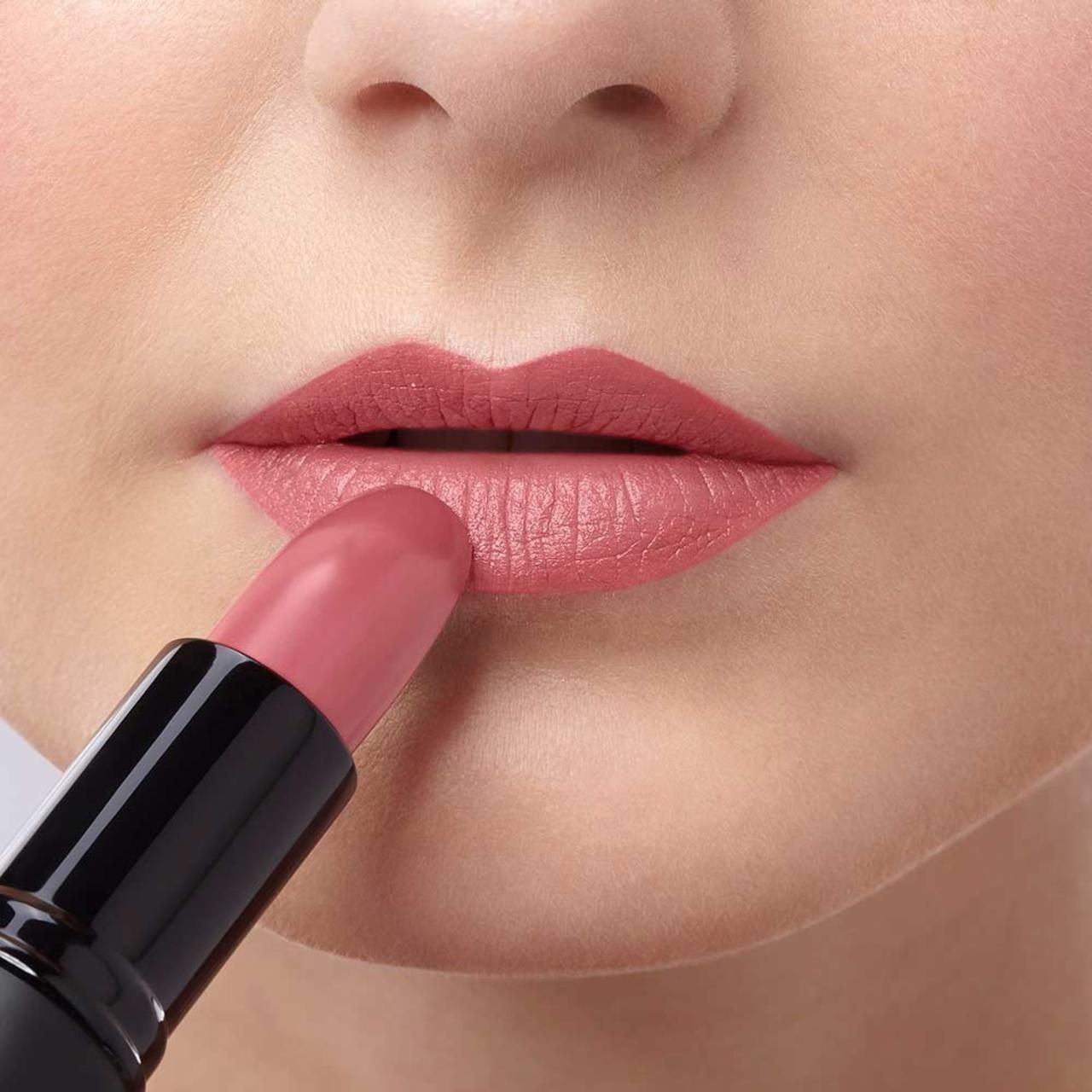Person trägt rosafarbenen Lippenstift auf den Lippen auf. Schwarzer Lippenstift-Halter sichtbar.