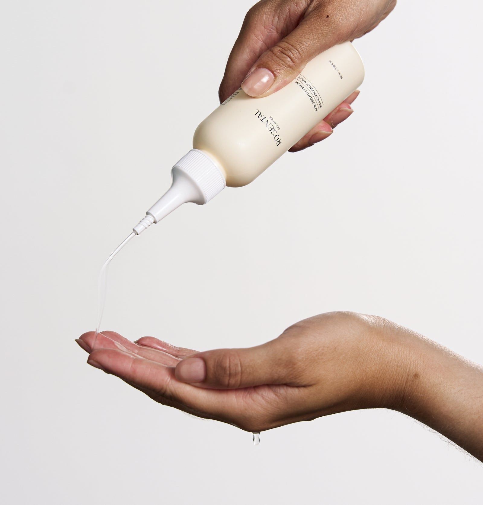 Person hält eine beige Flasche mit weißem Applikator. Flüssigkeit wird in die Hand gegossen. Produktname sichtbar.